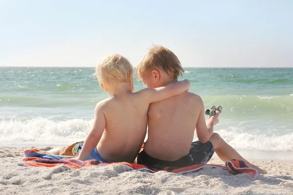 Jóvenes hermanos sentados en la playa junto al mar con los brazos alrededor de cada uno O — Foto de Stock