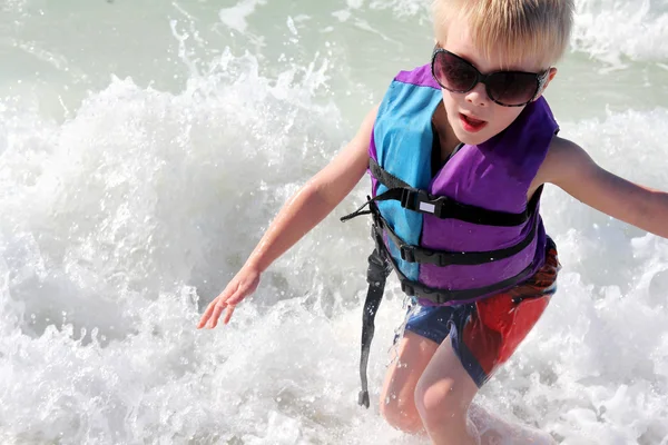 Jeune enfant jouant dans les vagues de l'océan en gilet de sauvetage — Photo