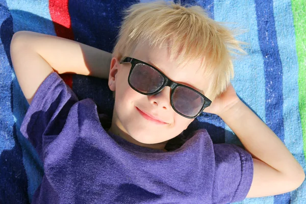 Feliz niño pequeño relajante en la toalla de playa con gafas de sol —  Fotos de Stock