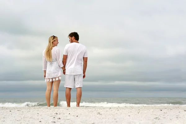 Szczęśliwa para trzymając się za ręce nad brzegiem oceanu przy plaży — Zdjęcie stockowe