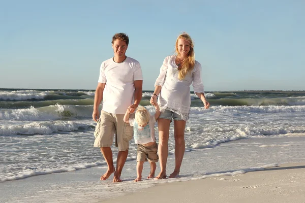 Familia feliz de tres personas caminando en la playa a lo largo del océano —  Fotos de Stock