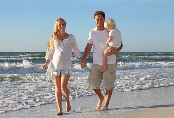 Familia feliz de tres personas caminando en la playa a lo largo del océano — Foto de Stock