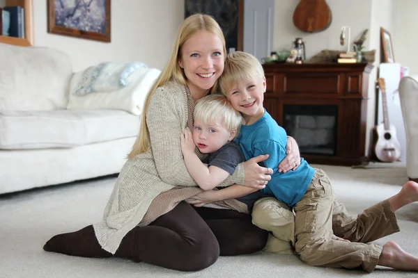 在家里抱着她的两个年轻孩子的幸福母亲 — 图库照片
