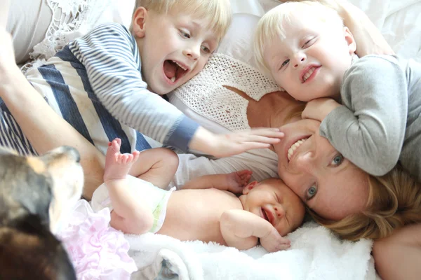 Felice giovane madre e tre bambini coccole sul letto — Foto Stock