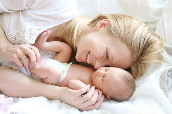 Feliz joven madre acurrucarse bebé recién nacido hija en la cama —  Fotos de Stock