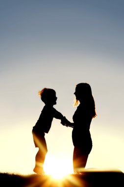Anne ve genç çocuk günbatımında elele silüeti