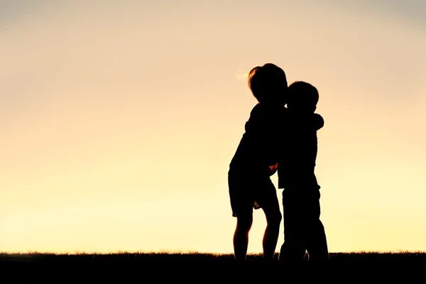 Silhouette di due bambini che si abbracciano al tramonto — Foto Stock