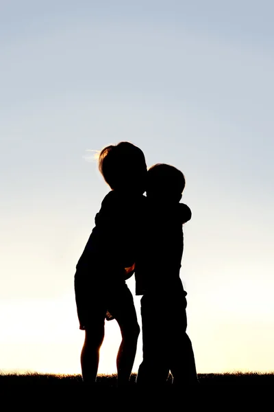 两个年幼的孩子拥抱在日落时的剪影 — 图库照片