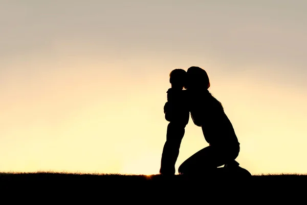 Silueta de madre joven abrazando a hijo pequeño al atardecer — Foto de Stock