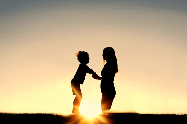 Silhouette de la mère et du jeune enfant tenant les mains au coucher du soleil — Photo