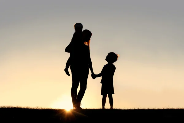母亲和年幼的孩子，手牵着手在日落时的剪影 — 图库照片
