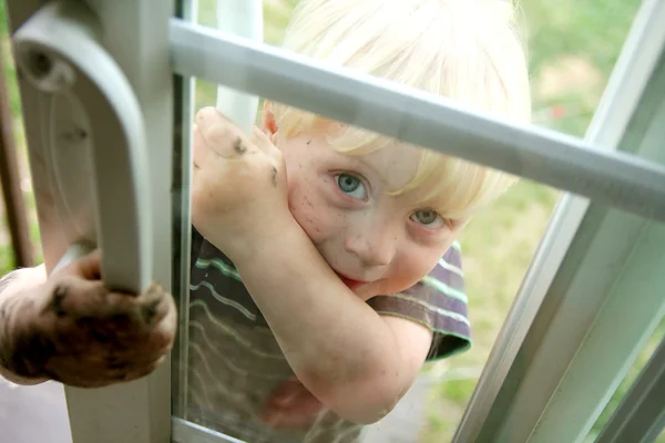 Sujo pouco menino espreitando no janela — Fotografia de Stock