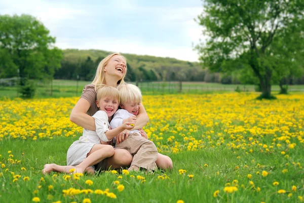 Mor och unga barn sitter i blomma äng skrattar — Stockfoto