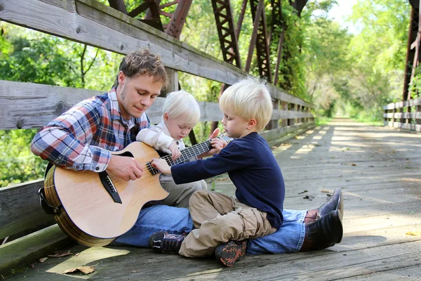 Vater und zwei Kinder spielen draußen im Park Gitarre — Stockfoto