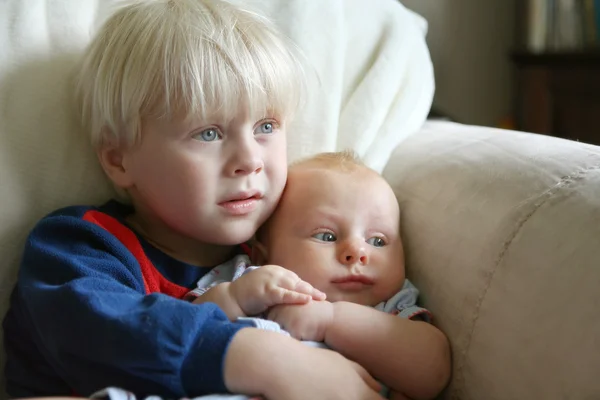Hermano pequeño sosteniendo a la hermana bebé en el sofá —  Fotos de Stock