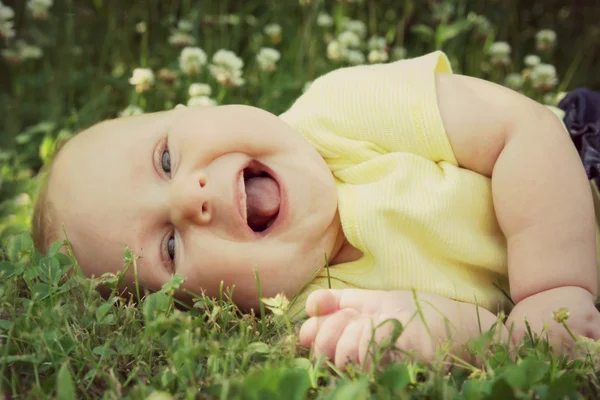 Pausbäckig lachendes Baby-Mädchen liegt draußen auf der Blumenwiese — Stockfoto