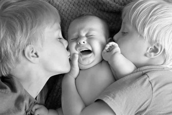 Jóvenes hermanos besos su llorando recién nacido bebé hermana —  Fotos de Stock