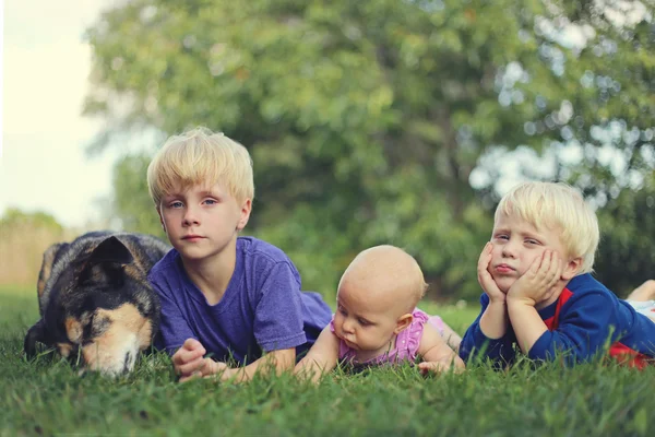 Tres niños pequeños aburridos y perro relajante fuera — Foto de Stock
