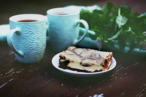 Curd dessert with a cup of tea on a dark background, decorated with sprigs of fresh mint. Breakfast in the fresh air.Composition in the rustic style, a combination of colors, brown and turquoise