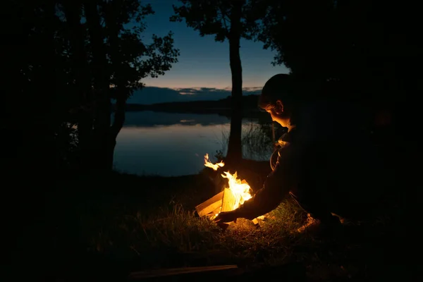 The silhouette of a girl by the fire on the lake. summer evening on the lake shore. night shooting, soft focus. advertising of tourist companies and fishing accessories. the concept of recreation