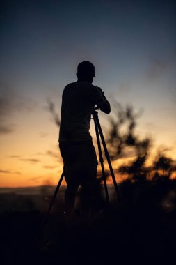Vahşi yaşam fotoğrafçısının silueti ayın altında gün batımında çalışıyor.