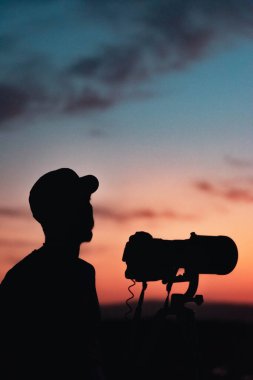 Vahşi yaşam fotoğrafçısının silueti ayın altında gün batımında çalışıyor.