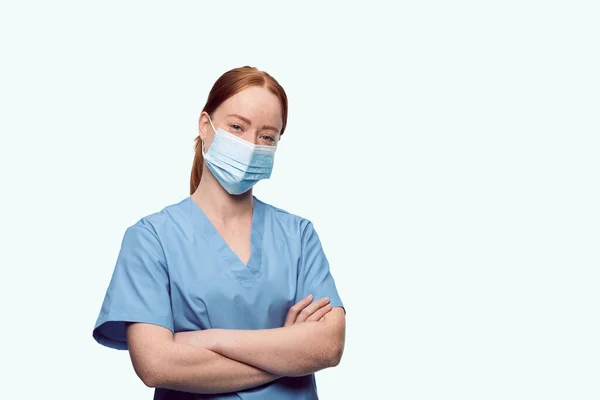 Jovem enfermeira ruiva com máscaras faciais olhando para a câmera — Fotografia de Stock