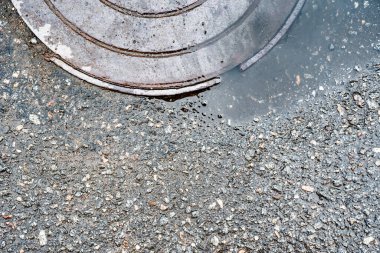 Yolda rögar kapağı olan eski bir asfalt. Yağmurdan sonra. 