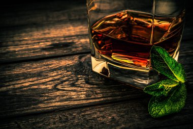 Eski ahşap bir masanın üzerinde nane filizi ile bir bardak brendi..  