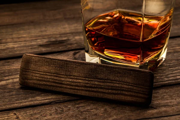 Eski ahşap bir masanın üzerinde boş ahşap bir kalasla bir bardak brendi.