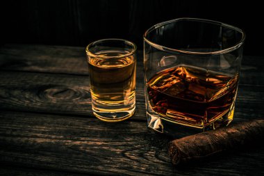 Eski ahşap bir masada Küba purosuyla bir bardak brendi ve tekila.