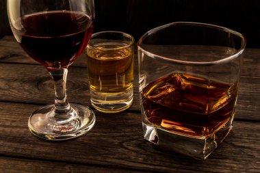 Üç bardak brendi, tekila ve kırmızı şarap eski bir ahşap üzerine.