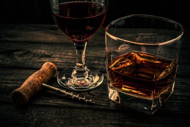 Eski ahşap bir masada tirbuşonlu bir bardak brendi ve kırmızı şarap.