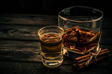 Glass of brandy and tequila with cinnamon sticks tied with jute  on an old wooden table 