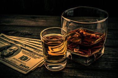 Glass of brandy and tequila with money on an old wooden table. 