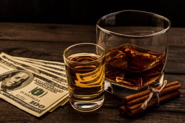 Glass of brandy and tequila with money and cinnamon sticks tied on an old wooden table 