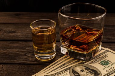 Glass of brandy and tequila with money on an old wooden table. 