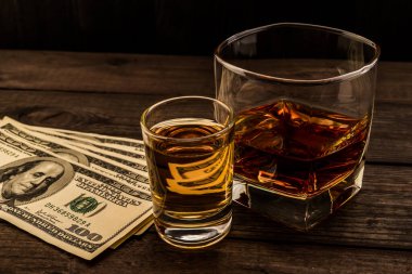 Glass of brandy and tequila with money on an old wooden table.