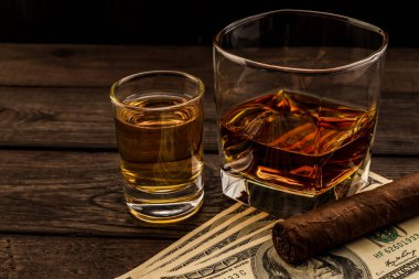 Glass of brandy and tequila with money and cuban cigar on an old wooden table 