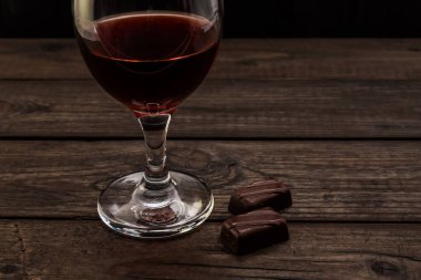 Glass of red wine with chocolate on an old wooden table. 