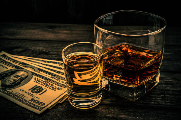 Glass of brandy and tequila with money on an old wooden table. 