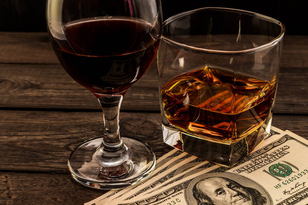Glass of brandy and red wine with money on an old wooden table. 