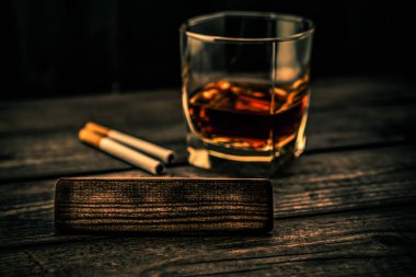 Glass of brandy with cigarettes and the empty wooden plank on an old wooden table 