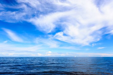 lake with white sailboat on horizon under cloudy sky