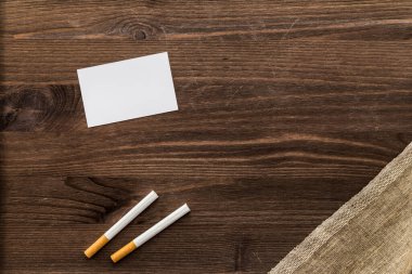 Empty card for notes with cigarettes and piece of canvas on an old wooden table 