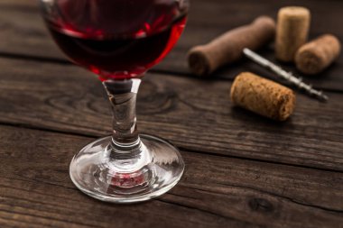 Glass of red wine and corkscrew with corks on an old wooden table