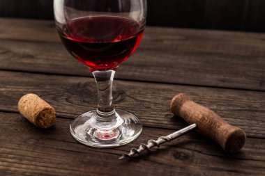 Glass of red wine and corkscrew with cork on an old wooden table