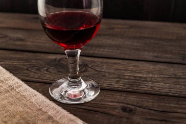 Bir bardak kırmızı şarap ve eski ahşap bir masanın üzerinde bir parça tuval..