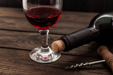 Bir şişe kırmızı şarap ve eski ahşap bir masada tirbuşon.