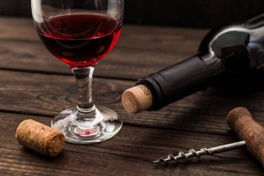 Bottle of red wine with a glass and corkscrew with cork on an old wooden table 